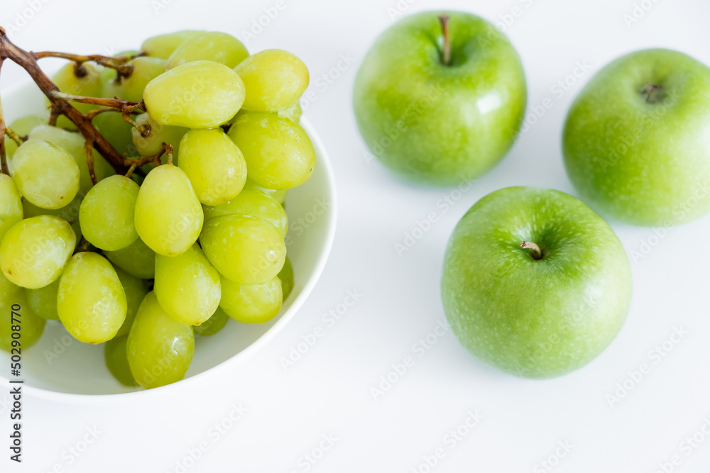 top view of grapes in bowl near apples on white.