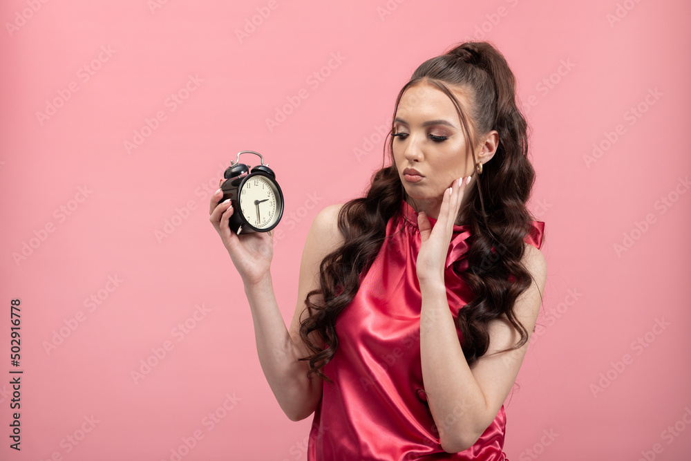 Fototapeta premium Time Pressure. Stressed woman holding clock, looking anxiously at passing time, isolated on pink background. Human face expression emotion reaction. Fatigue headache overwork.