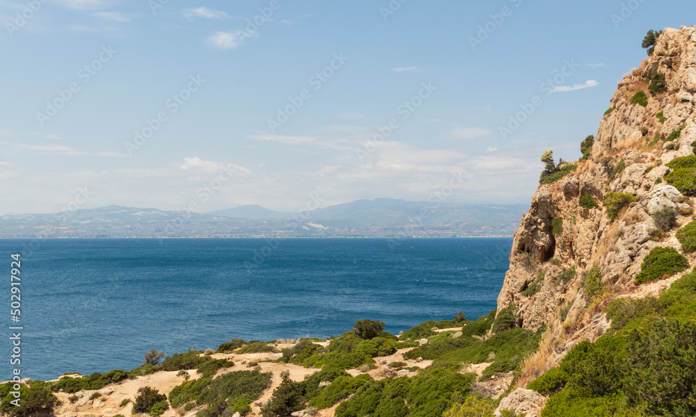 Mediterranean sea and steep rugged cliffs, clear sky and mountains are on the background. Greece