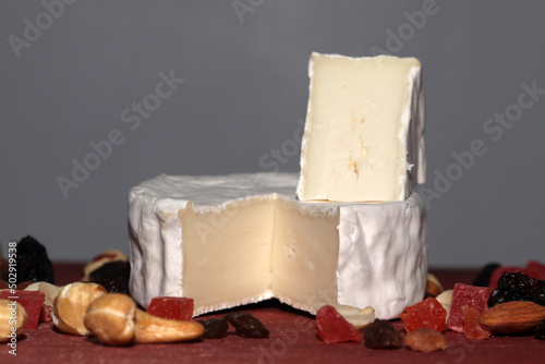 cut brie cheese with nuts and dried fruits on a wooden table and with a gray wall