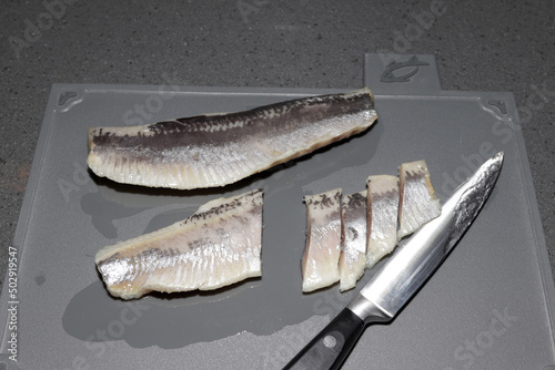 salted herring fillet whole and cut with a knife on a gray board