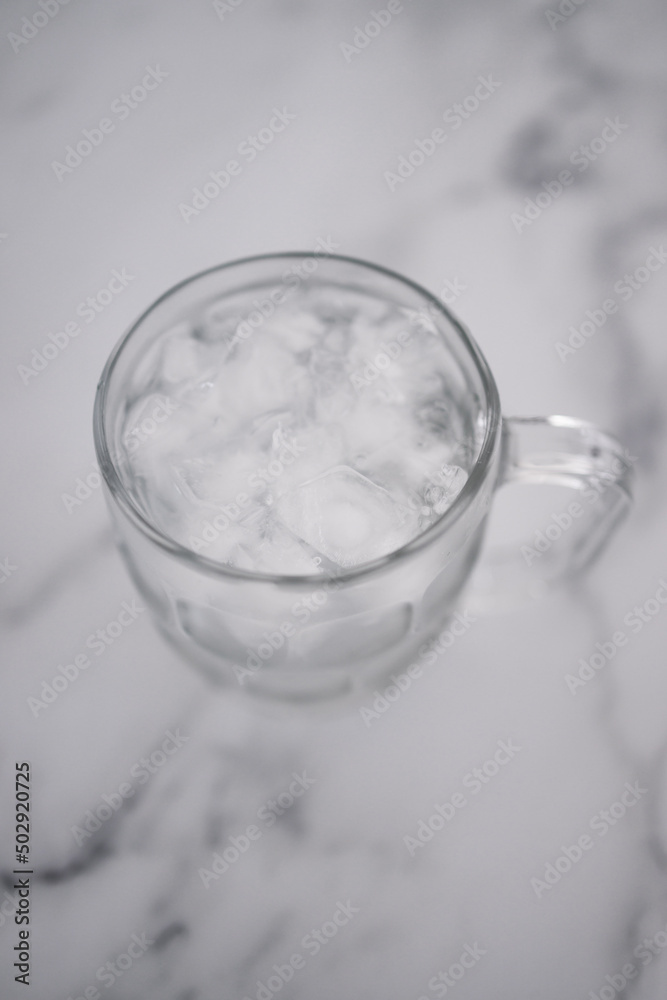 drinking enough water or sobriety concept, pint glass with tap water and ice cubes over marble background drinking enough water or sobriety concept, pint glass with tap water and ice cubes over marble background
