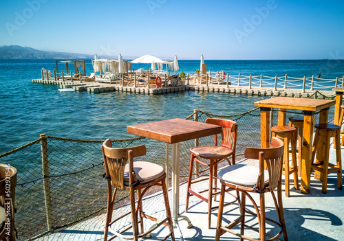 Resting area with artificial floating island and tables and chairs on relaxing public beach of the Red Sea, Middle East. Concept of bliss and happy vacation