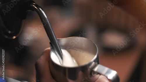 Process of preparing milk foam for cappuccino or latte, heating and whipping. Barista steaming milk in the pitcher. slow motion.