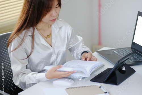 Businesswoman working on laptop computer and reading a business book