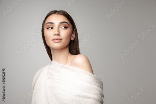 Portrait of tender young woman covered with white veil isolated over grey background. Natural beauty