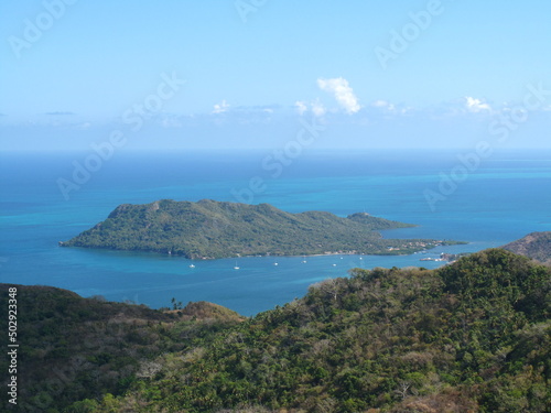 Ile montagneuse des Caraïbes, vue depuis le continent dans un environnement verdoyant et arboré, entourée d'une mer bleu vif et d'un ciel bleu avec quelques nuages blancs