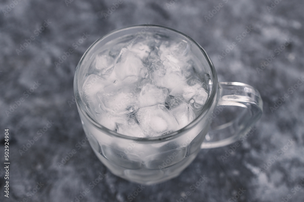 drinking enough water or sobriety concept, pint glass with tap water and ice cubes over grey concrete