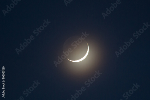 Color photograph of a young growing moon against a dark sky. The ashen light of the Moon and the bright edge of the Earth's night satellite.