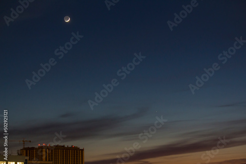 Color photograph of a young waxing moon and the planet Mercury against a dark blue sky. The ashen light of the moon. Astronomy.