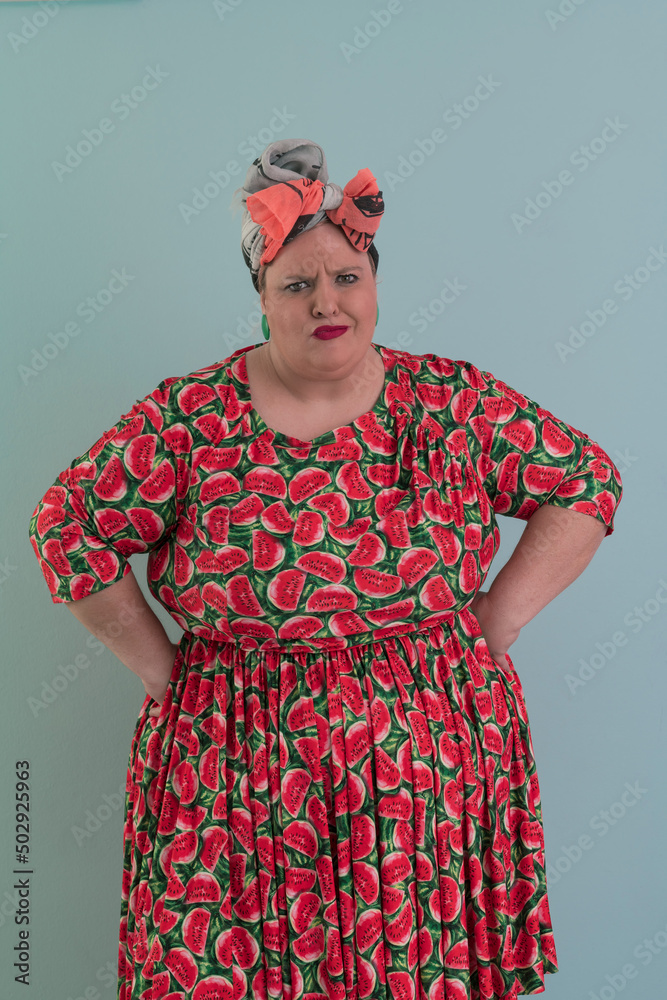 Fototapeta premium Plus size sexy model woman with trendy makeup, fashionable blonde in colorful dress posing at the cyan or light blue background in studio.