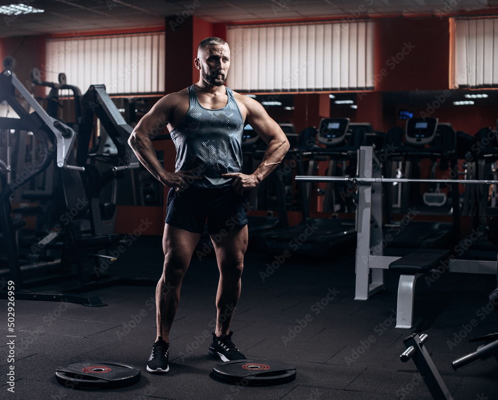 Fototapeta premium Serious sports man standing and posing in gym and looking aside.