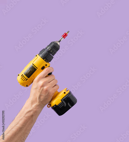 Man hand holds Brushless Cordless Combi Drill that comes from corner on purple color background