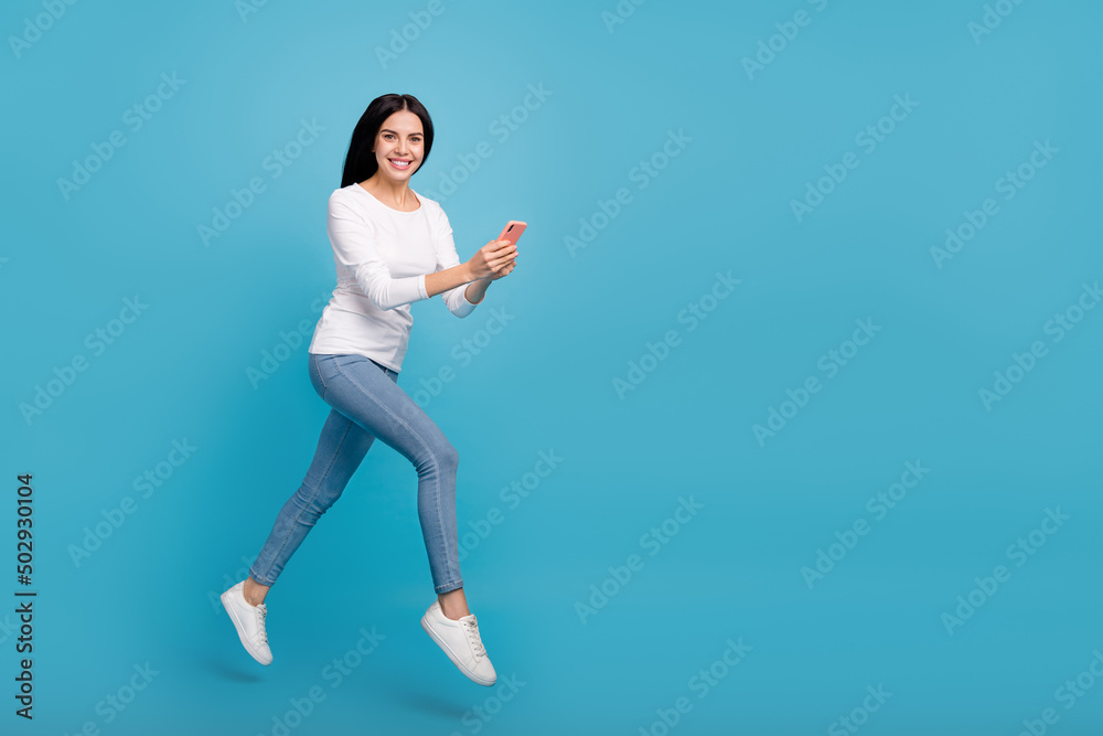 Full length body size view of beautiful trendy cheery girl jumping using gadget app 5g isolated on bright blue color background Full length body size view of beautiful trendy cheery girl jumping using gadget app 5g isolated on bright blue color background
