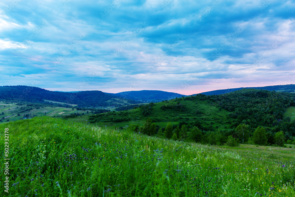 Mountain landscape with green field and blue clouds before sunrise.
