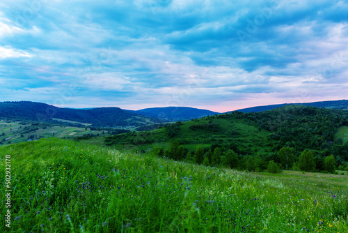 Mountain landscape with green field and blue clouds before sunrise.