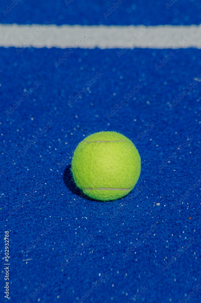 blue paddle tennis court, a single ball near the baseline