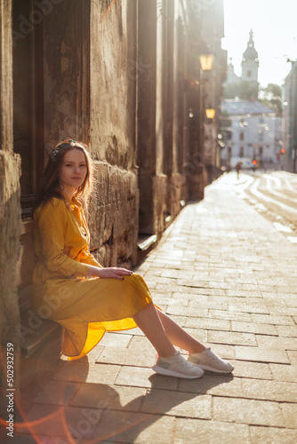 Stylish girl in yellow dress sitting on old city street