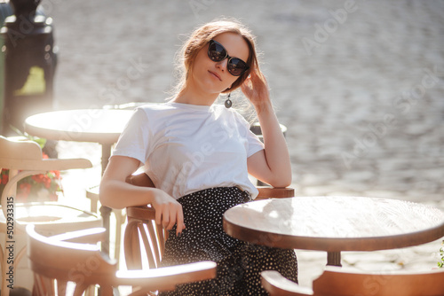 Stylish girl in sunglasses, white t-shirt and polka-dot skirt relax on the summer terrace