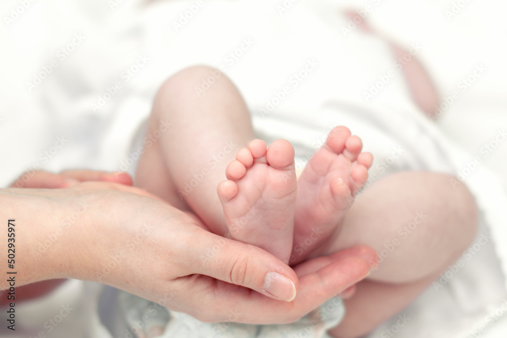 The mother's hands tenderly and lovingly hold the legs of a small child who is several months old from the moment of birth.