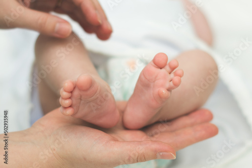 The mother's hands tenderly and lovingly hold the legs of a small child who is several months old from the moment of birth.