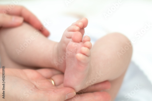 The mother's hands tenderly and lovingly hold the legs of a small child who is several months old from the moment of birth.
