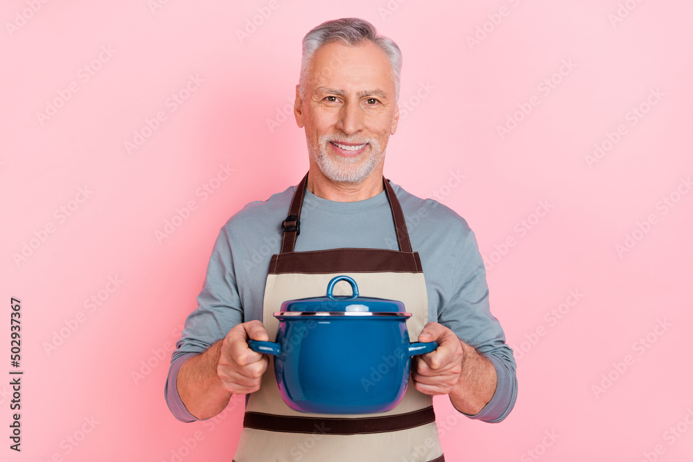 Photo of good mood man pensioner dressed grey shirt apron holding saucepan isolated pink color background
