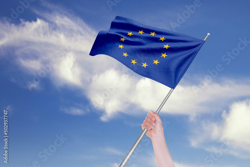 Female Hand is Waving European Union Flag Against Blue Sky with Clouds