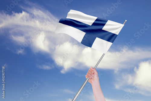 Female Hand is Waving Finnish Flag Against Blue Sky with Clouds