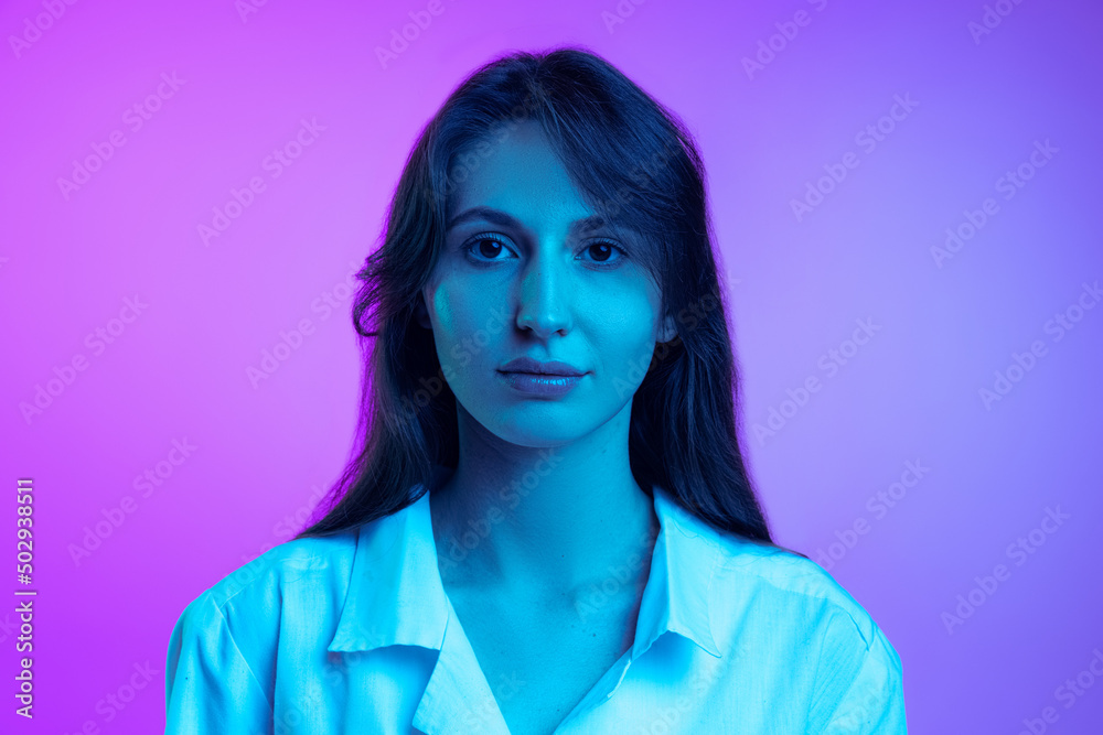 Young beautiful woman in white shirt isolated over purple studio background in neon light. Concept of emotions, facial expression, art, beauty Young beautiful woman in white shirt isolated over purple studio background in neon light. Concept of emotions, facial expression, art, beauty