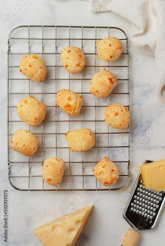 Freshly baked homemade cheese buns on a baking rack on a light marble background close-up. Brazilian cheese bread. A gourmet snack. Delicious pastries. Selective focus, top view