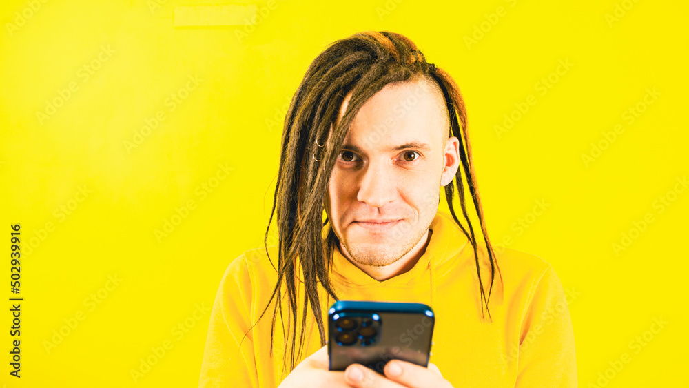 Young happy man browsing mobile phone on yellow background. Portrait of handsome positive male in yellow hoodie using smartphone. Young happy man browsing mobile phone on yellow background. Portrait of handsome positive male in yellow hoodie using smartphone.