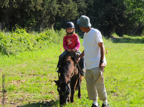 young girl riding poney with father helping on sunny day hobby or activity during holidays .