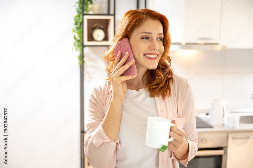 Beautiful red haired ginger woman drinking coffee and talking on mobile phone in bright apartment. Beautiful red haired ginger woman drinking coffee and talking on mobile phone in bright apartment.