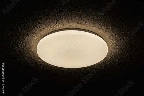 one chandelier from a round white shade with lighting on a gray black ceiling in a dark room