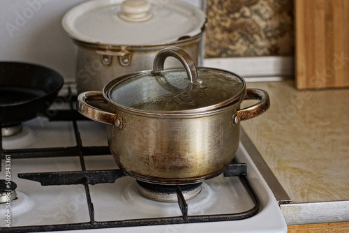 a one gray dirty metal saucepan with a lid on the stove