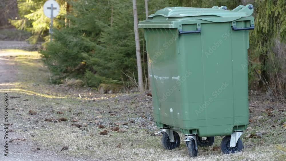A green garbage bin on the side of the bushes in the forest in Estonia A green garbage bin on the side of the bushes in the forest in Estonia