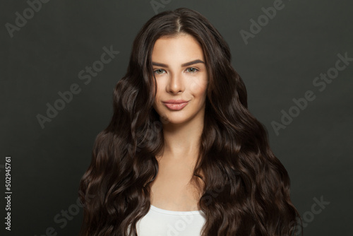 Cute woman with long curly beautiful hair smiling on black background