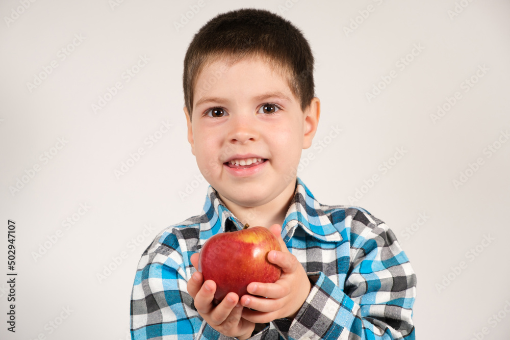 A 4-year-old preschool boy with red apple in his hands is smiling against a white background. A 4-year-old preschool boy with red apple in his hands is smiling against a white background.