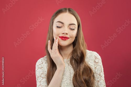 Pretty young happy woman with long brown hair and red lips makeup on red studio background