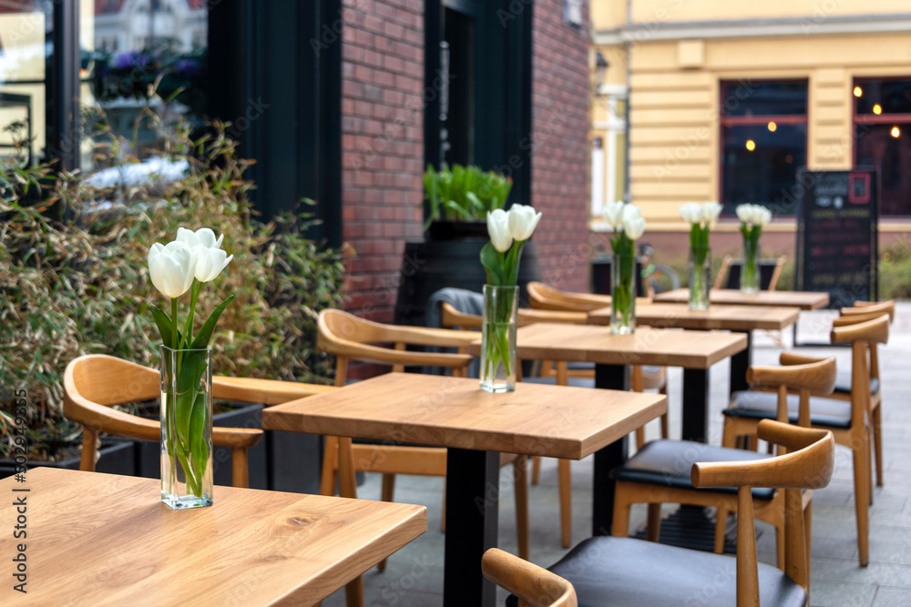 Empty tables with flowers in outdoor cafe or restaurant. Tables and chairs at sidewalk cafe. Touristic setting, tulips on cafe table, sidewalk cafe furniture. Empty tables with flowers in outdoor cafe or restaurant. Tables and chairs at sidewalk cafe. Touristic setting, tulips on cafe table, sidewalk cafe furniture.