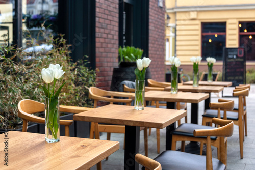 Empty tables with flowers in outdoor cafe or restaurant. Tables and chairs at sidewalk cafe. Touristic setting  tulips on cafe table  sidewalk cafe furniture.