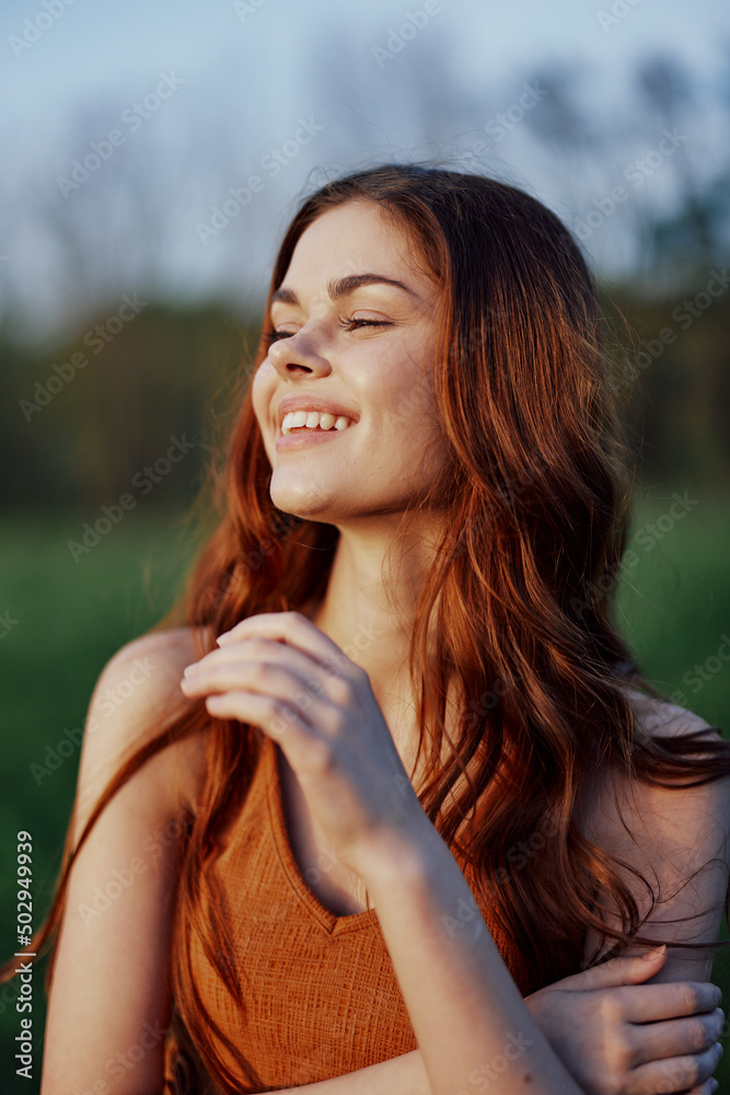 Portrait of a woman with a beautiful smile in summer green nature against the grass, looking out at the setting sun. The concept of health and beauty Portrait of a woman with a beautiful smile in summer green nature against the grass, looking out at the setting sun. The concept of health and beauty