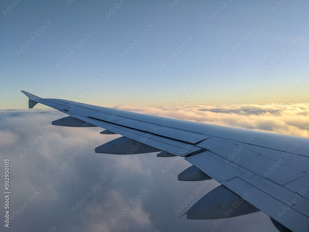 airplane wing during a flight, golden sunset sky and clouds