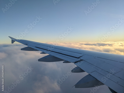 airplane wing during a flight, golden sunset sky and clouds