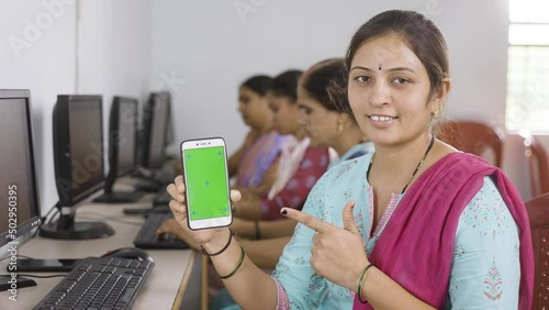 Happy women showing green screen mobile phone by pointing finger while lookingcamera at computer class - concept of online booking, advertisement and education photo