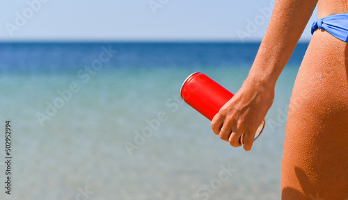 The girl holds in her hand a red can with a cold drink on the background of the sea.