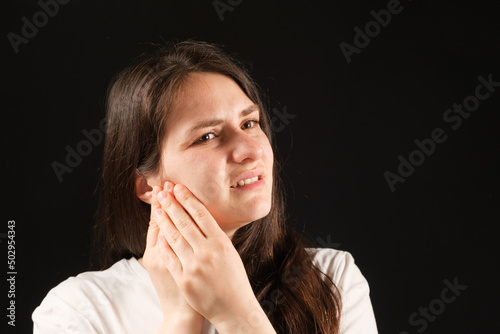 A woman holds her hands to a sore temporomandibular joint, dysfunction and pain, dislocated jaw, problems of wisdom teeth.