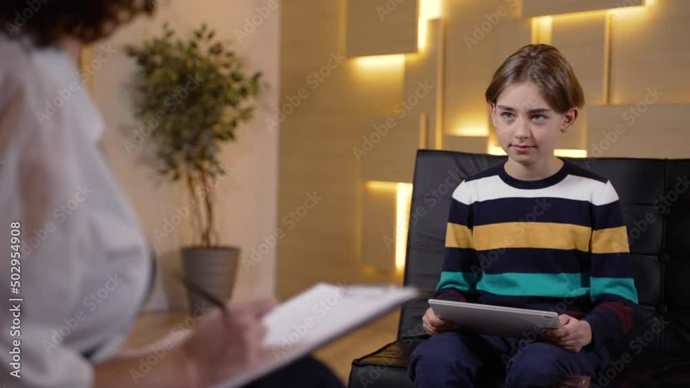 Boy patient looking at drawings on tablet and explaining what he sees to child counselor during psychological testing. Female child psychotherapist testing little patient during consultation Boy patient looking at drawings on tablet and explaining what he sees to child counselor during psychological testing. Female child psychotherapist testing little patient during consultation