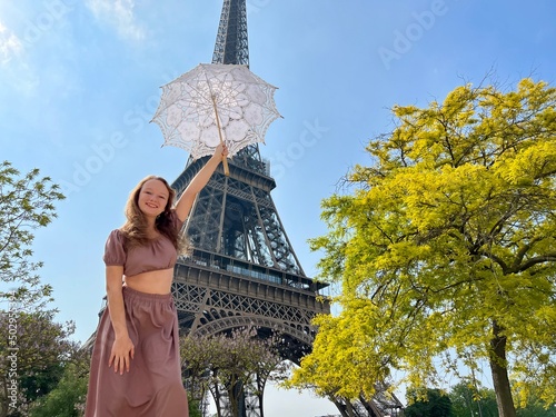 a girl with a white parasol stands against the backdrop of the Eiffel Tower with her back to us can be used for advertising for the Internet for travel agencies. High quality photo © Oleksandra